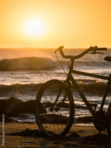 Fototapeta Naklejka Na Ścianę i Meble -  bicicleta sobre la arena al atardecer con el sol y el mar detrás