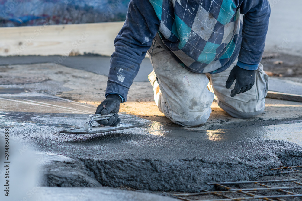 Close up on midsection of unknown worker spreading concrete cement mortar on the ground in day at construction site Close up on midsection of unknown worker spreading concrete cement mortar on the ground in day at construction site