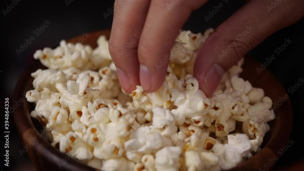 Closeup man hand taking popcorn from wood bowl. Eating pop corn at home Closeup man hand taking popcorn from wood bowl. Eating pop corn at home