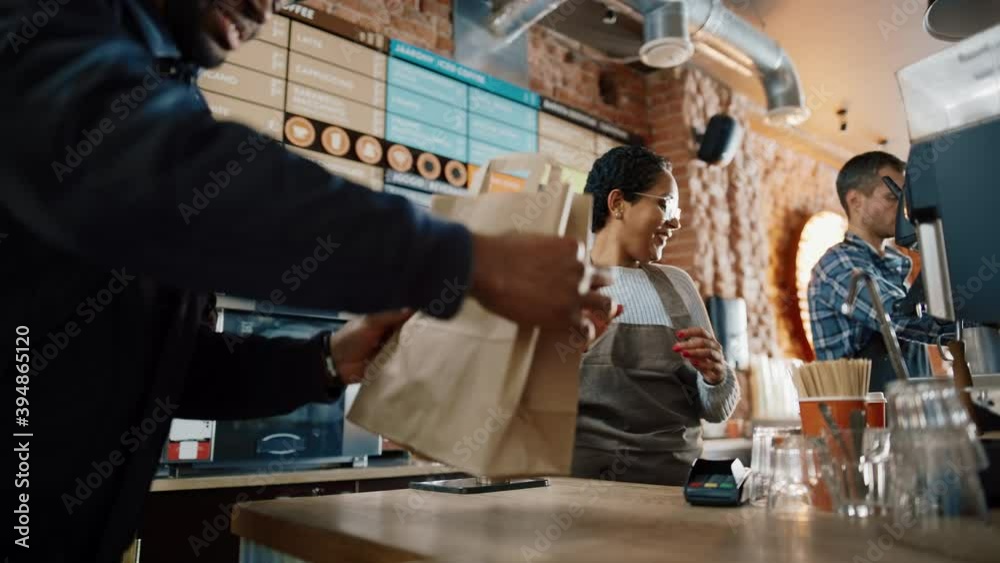 Friendly Latin Barista Serves Order to a Food Delivery Courier Picking Up Two Take Away Coffees and Pastries from a Cafe Restaurant. Delivery Guy Puts Food in His Hot Thermal Insulated Bag.