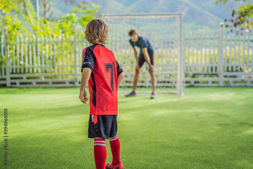 Obraz premium Little cute kid boy in red football uniform and his trainer or father playing soccer, football on field, outdoors. Active child making sports with kids or father, Smiling happy boy having fun in