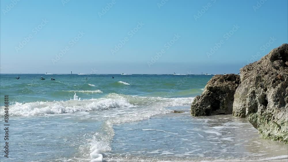 Waves crashing on rocks, Brown Pelicans (Pelecanus occidentalis) diving, Jet Skis going across horizon.