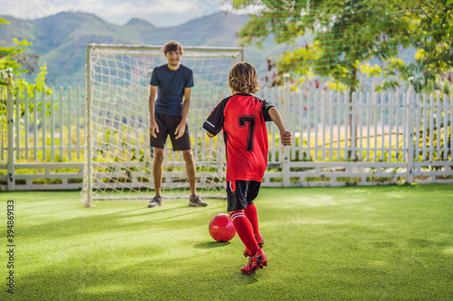 Little cute kid boy in red football uniform and his trainer or father playing soccer, football on field, outdoors. Active child making sports with kids or father, Smiling happy boy having fun in