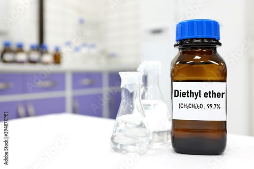 Selective focus of diethyl ether liquid chemical compound in dark glass bottle inside a chemistry laboratory with copy space.	 photo