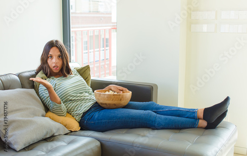 pretty woman looking surprised and shocked, with jaw dropped holding an object with an open hand on the side photo