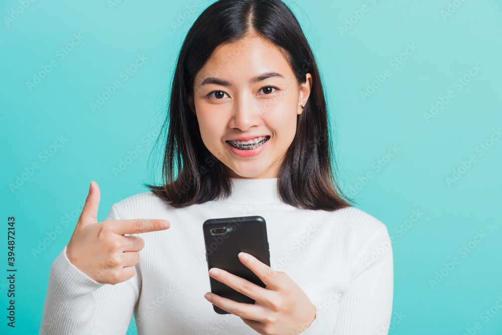 Beautiful Asian woman smile she pointing finger to a smartphone, female excited cheerful after received promotion her point finger on mobile phone isolated on a blue background, Technology concept Beautiful Asian woman smile she pointing finger to a smartphone, female excited cheerful after received promotion her point finger on mobile phone isolated on a blue background, Technology concept