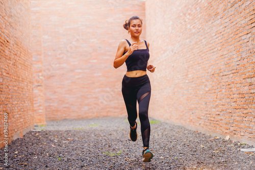 Fit young woman at start running. Runner start a race on a rock track with tall red brick wall as background.