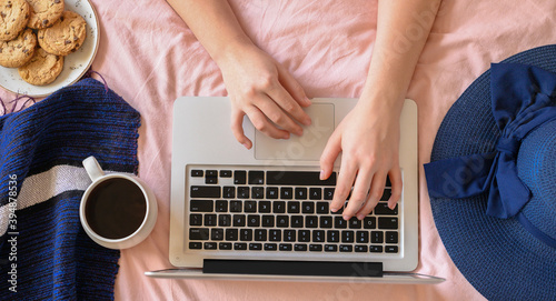 Young woman typing on laptop in bed. Lifestyle hero header with view from above with cup of caffe hat. Freelancer or fashion blogger home workspace