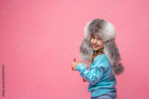 little girl in a white fur hat stands on pink background and shows the class