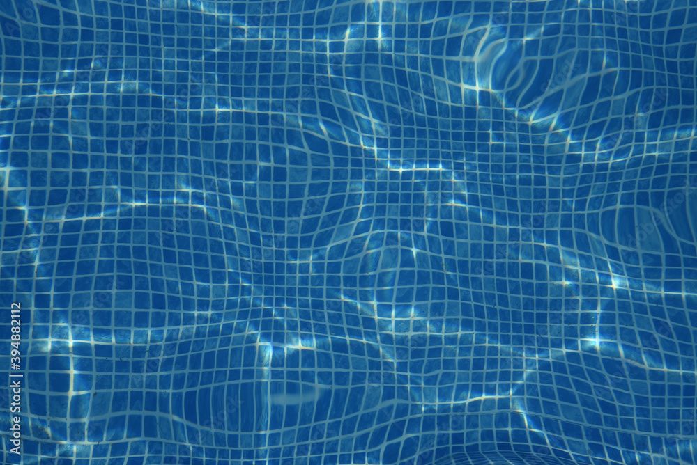 Small blue tiles in the pool. The bottom of the pool is visible through the clear water. Background, texture Small blue tiles in the pool. The bottom of the pool is visible through the clear water. Background, texture