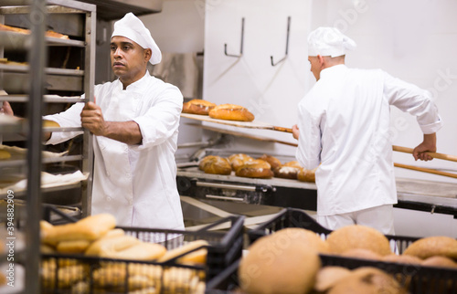 man in chefs uniform rolling trolley with bread in bakery