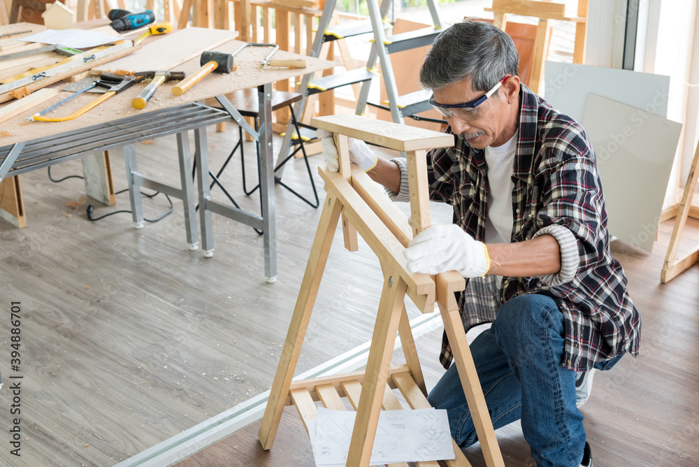 Senior asian old man carpenter wearing glasses and gloves protection building diy furniture in workshop