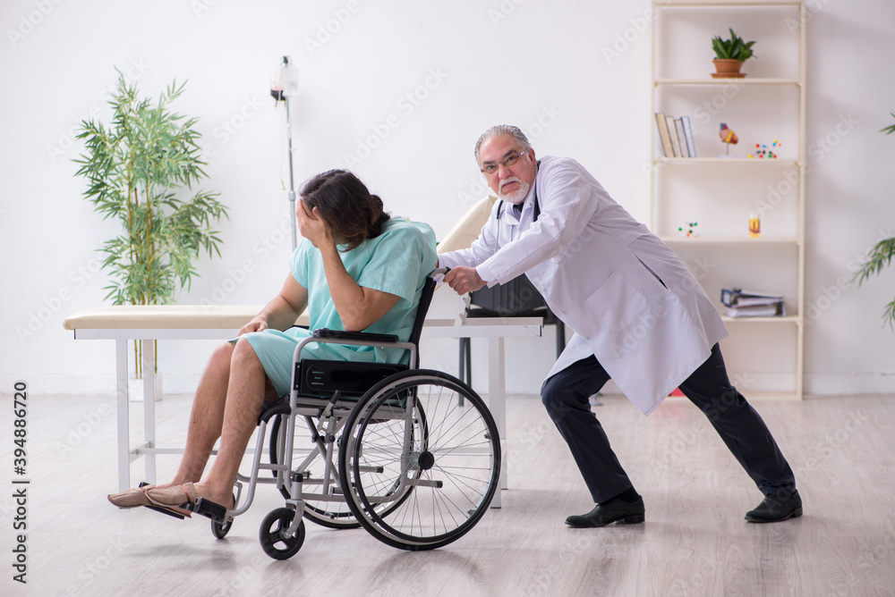 Young male patient in wheel-chair and experienced doctor traumatologist Young male patient in wheel-chair and experienced doctor traumatologist