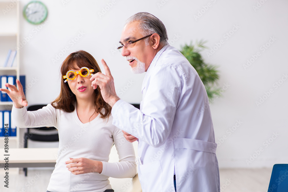 Fototapeta premium Young woman visiting old male doctor ophthalmologist