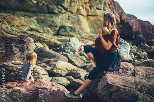 Mother with baby in sling watching her preschooler play on the rocks