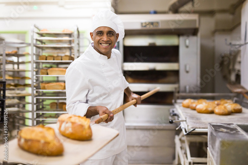 man in chefs uniform with bread on shovel in bakery