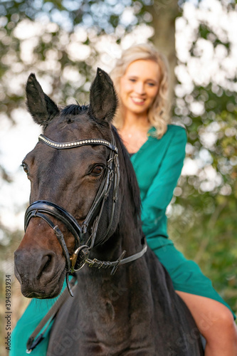 Portrait of a blonde girl in a vintage green dress with a big skirt posing with a brown horse. Selective focus © Dasya - Dasya