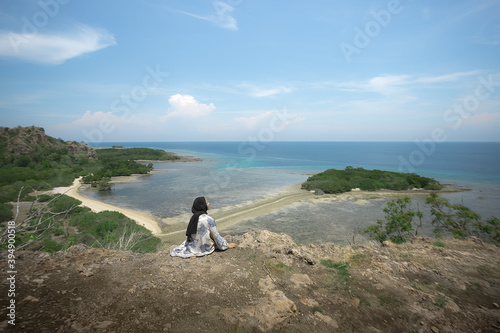 A young traveler girl sits on the edge of a hill on Balanan Beach and enjoys the beautiful sea view of Baluran National Park. Young girls love wildlife  travel  freedom.