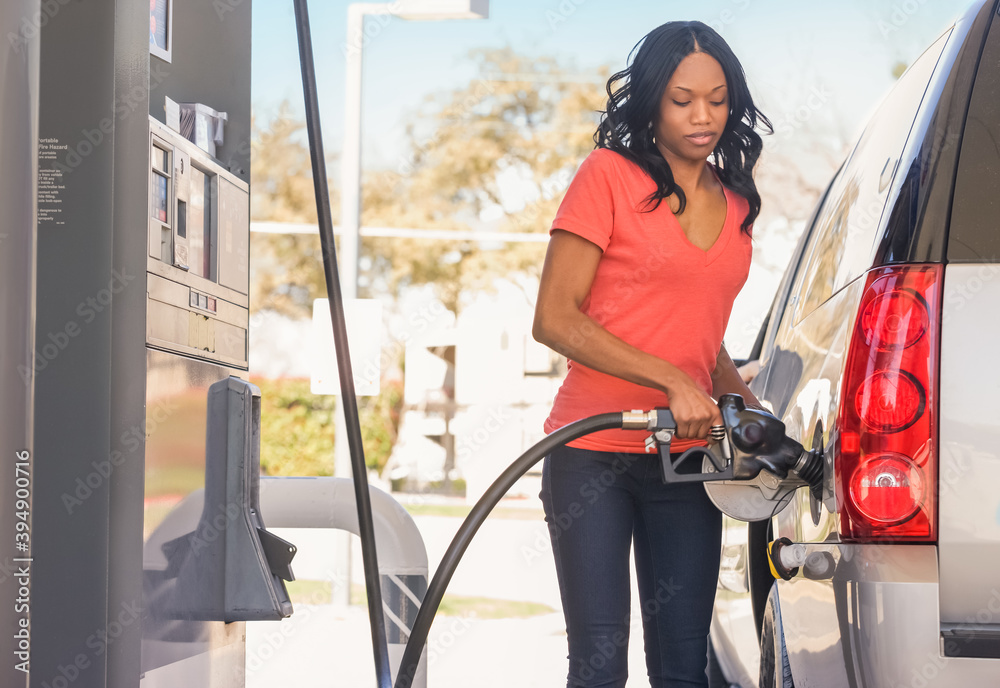 African American woman pumping gas at gas station foto de Stock Adobe