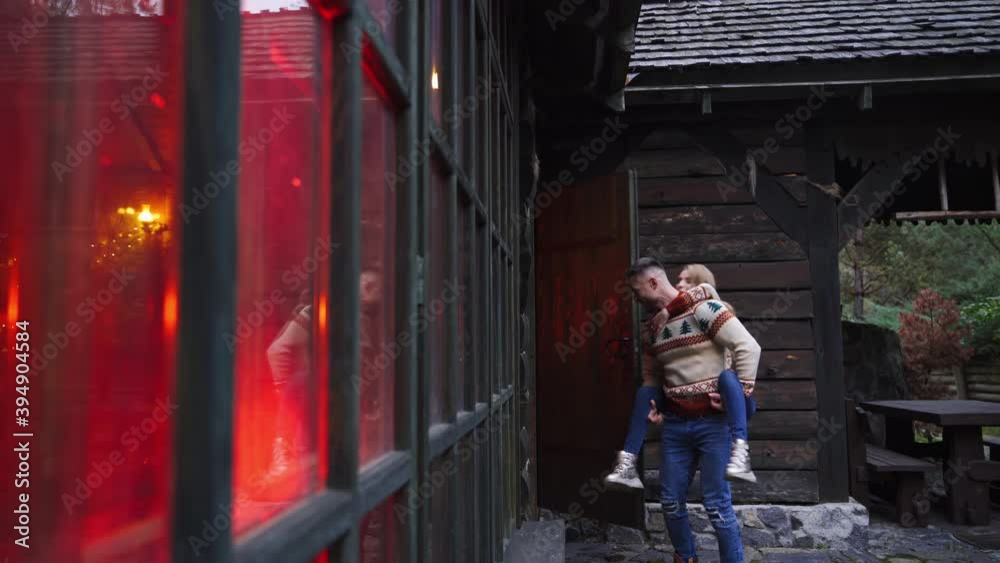 Love story. Dating outside. Young сouple on wooden house in forest background. Guy carries girl on his back. Love story. Dating outside. Young сouple on wooden house in forest background. Guy carries girl on his back.