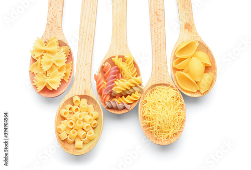 Spoons with different uncooked pasta on white background