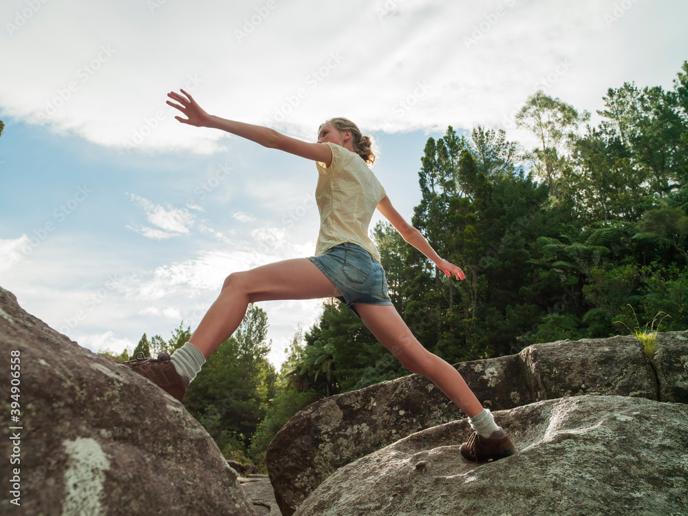 Female teenager stretching from one boulder to another in the wilderness Female teenager stretching from one boulder to another in the wilderness