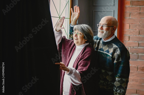 An elegant old couple in a Christmas studio. Grandparents in a cute sweaters. Family standing near window