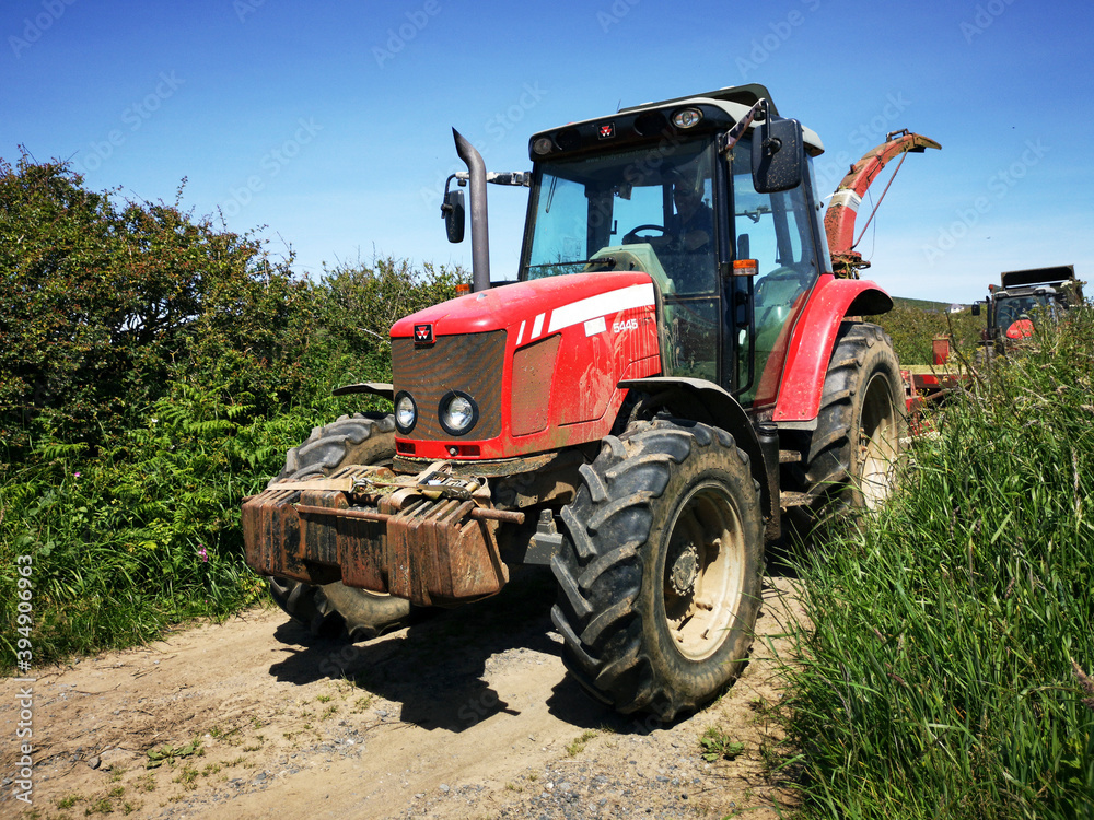 A tractor in a country lane with high hedges around the edge of a field. Rural farming concept during harvest season - UK A tractor in a country lane with high hedges around the edge of a field. Rural farming concept during harvest season - UK