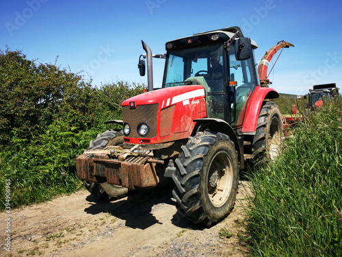 A tractor in a country lane with high hedges around the edge of a field. Rural farming concept during harvest season - UK