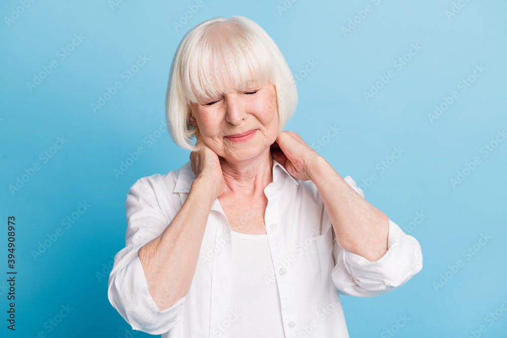 Photo portrait of grandmother touching neck having headache migraine need pills isolated on vivid blue color background Photo portrait of grandmother touching neck having headache migraine need pills isolated on vivid blue color background