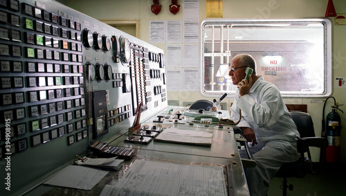 Senior engineer taking phone instructions whilst monitoring controls in ship's engine room. photo