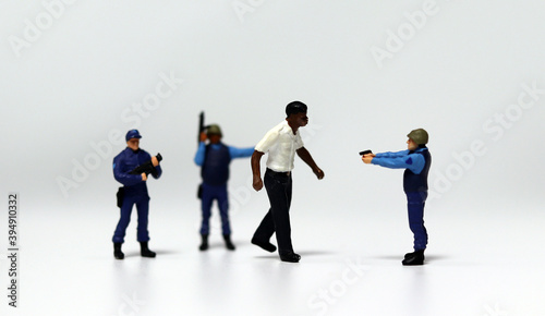 Fotografie A police miniature blocking a walking black miniature man and pointing a gun at him