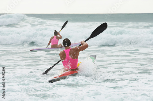 Back view of male and female surf lifesaver paddling through waves on ocean surf ski photo