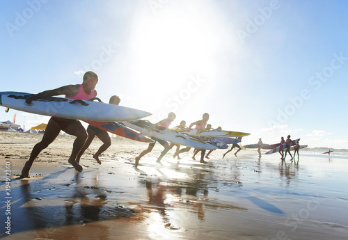 Team of male surf lifeguards training and running into sea holding ocean surf skis photo