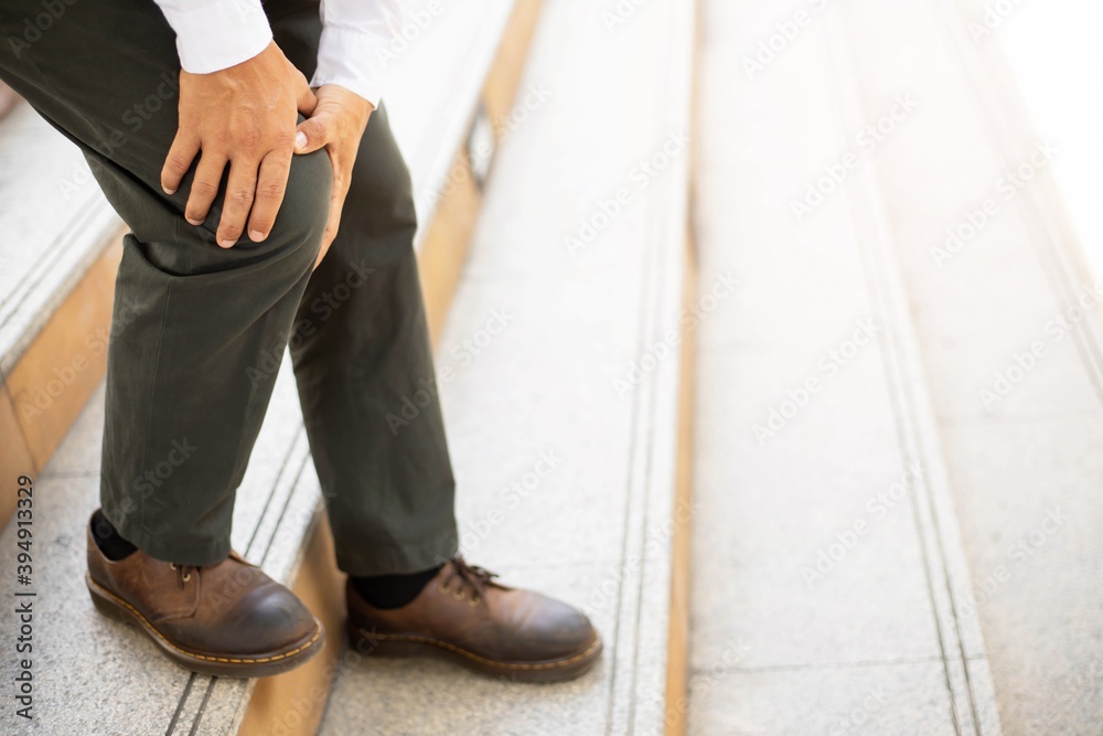 A man standing on the stairs have the sore pain and painful knee problem.walk up and down stairs accident. Health care concept. A man standing on the stairs have the sore pain and painful knee problem.walk up and down stairs accident. Health care concept.