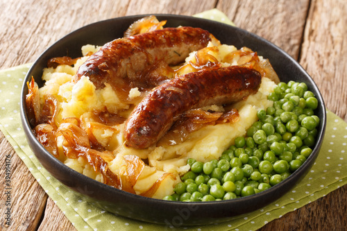 Tasty Bangers and Mash made of sausages served with mashed potatoes, green peas and onion gravy close-up in a plate on the table. Horizontal photo