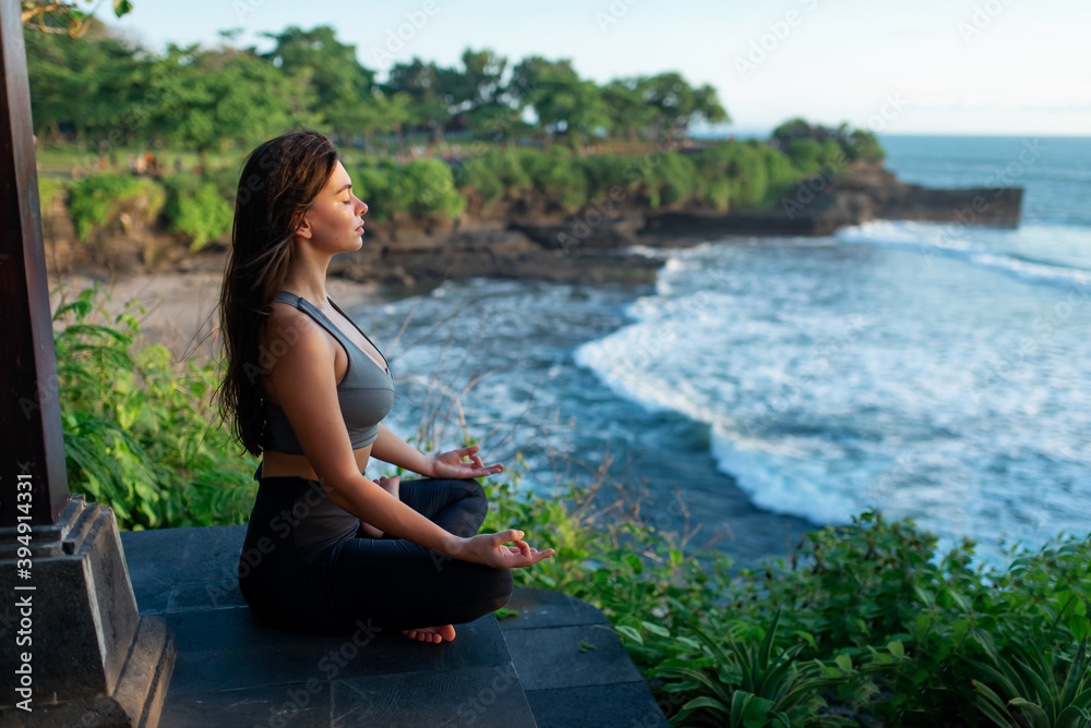 A young woman meditates by the sea.