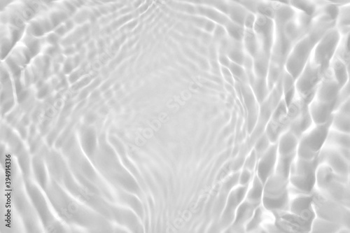 De-focused. Transparent clear calm water surface texture desaturated gray colored with splashes and bubbles. Trendy abstract nature background. Water waves in sunlight. Copy space for product mockup