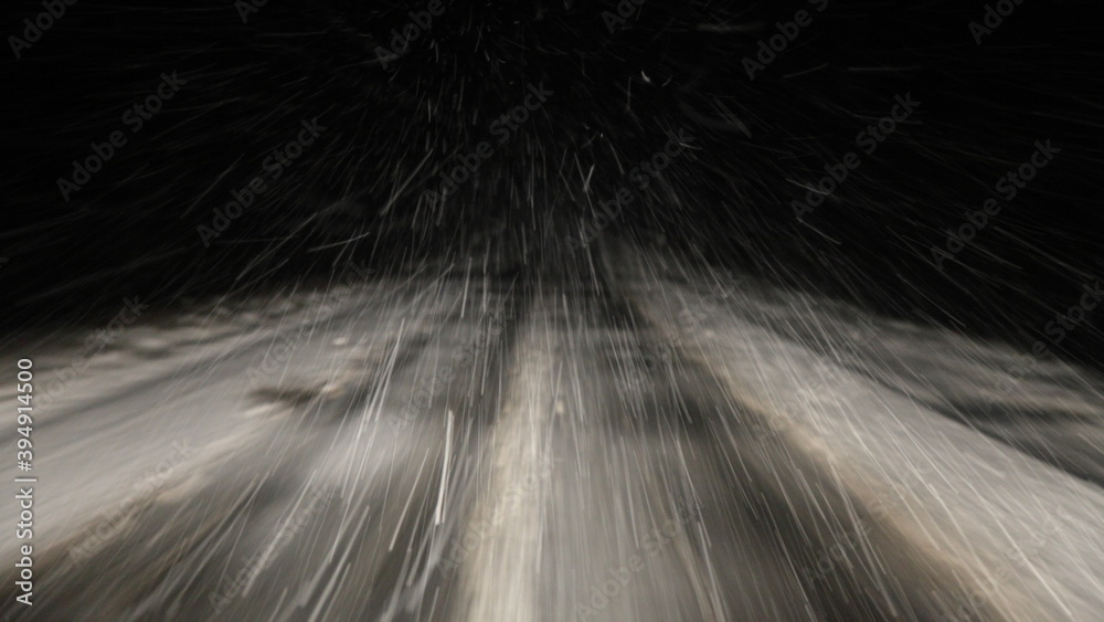 Heavy snowfall, snowstorm on a winter road at night, a car driving on a white highway track with insufficient visibility, a view of the motorway from driver's windglass from inside a moving vehicle
