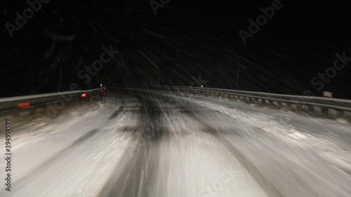 Heavy snowfall, snowstorm on a winter road at night, a car driving near highway roadside turn fence in perspective, a view of the motorway from the driver's seat from inside a moving vehicle photo