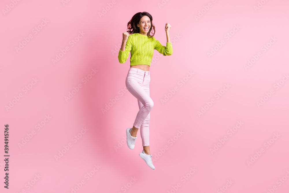 Full length photo of lucky wavy lady wear green sweater jumping high arms fists isolated pastel pink color background