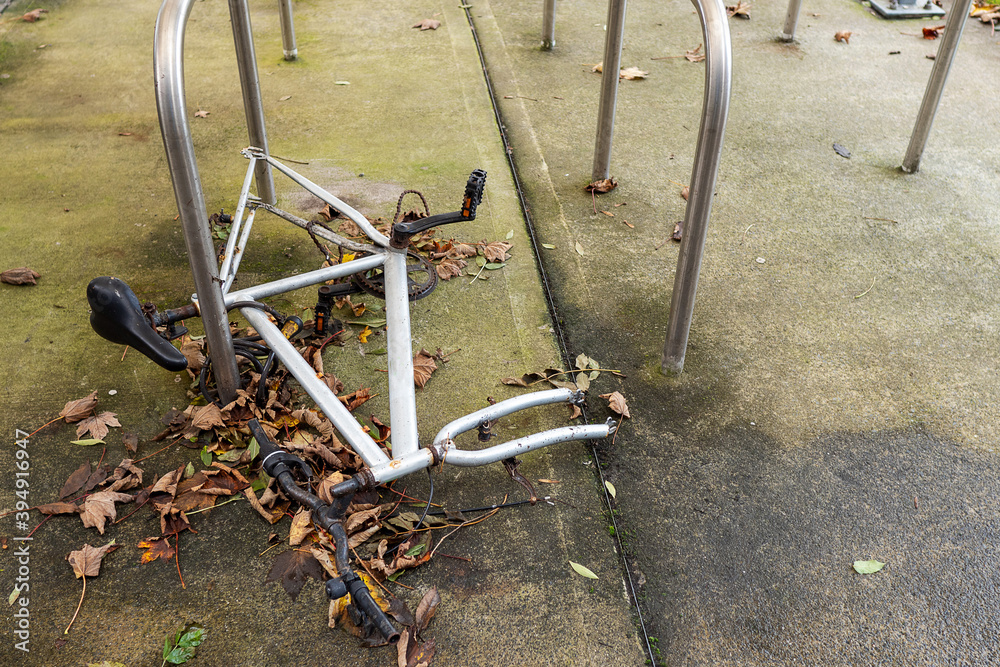 White frame of a bicycle on a ground attached to bicycle stand by metal chain stripped of wheels. Modern urban crime and lack of security concept.