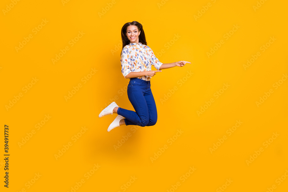 Full length photo portrait of girl pointing two fingers at blank space jumping up isolated on vivid yellow colored background Full length photo portrait of girl pointing two fingers at blank space jumping up isolated on vivid yellow colored background