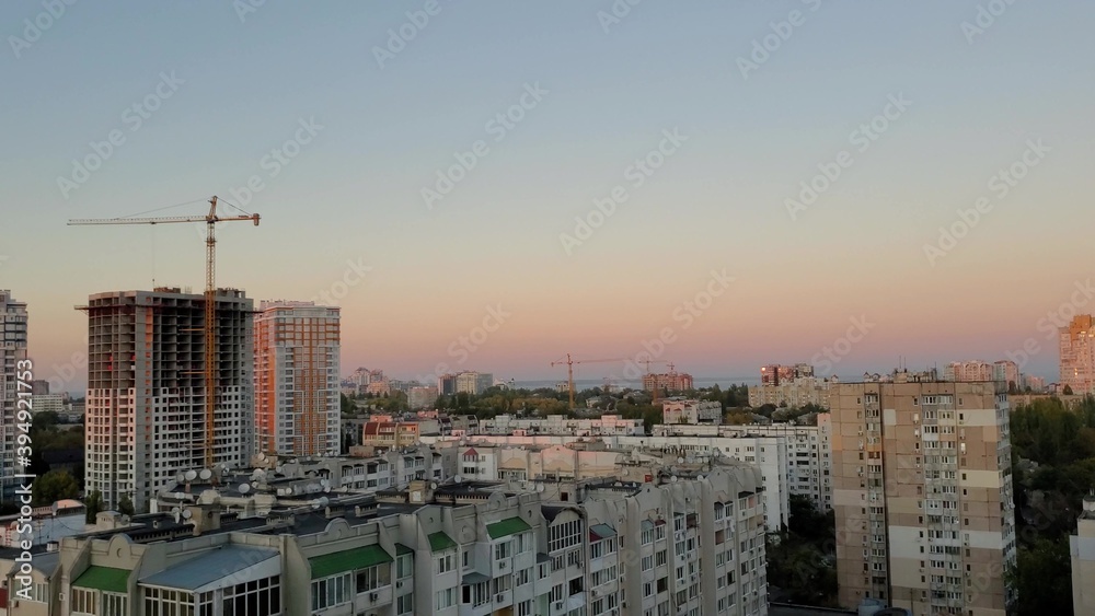Aerial urban view with dusk sky. Urban skyline with construction crane near unfinished skyscraper with clear dusk sky. Under construction concept of real estate development. Residential district