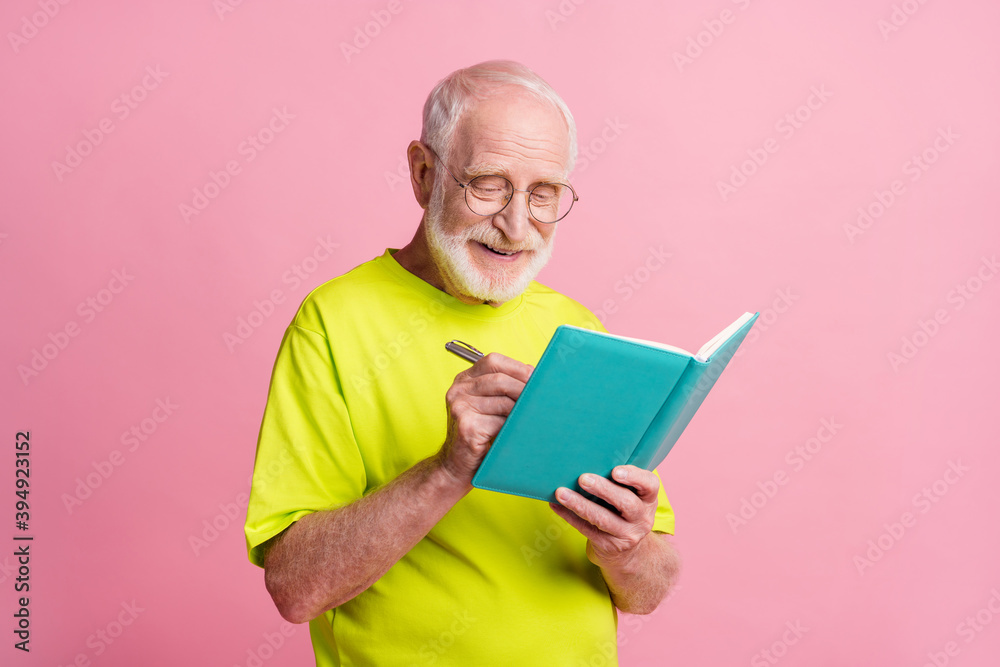 Portrait of optimistic pensioner write copybook wear spectacles green color t-shirt isolated on pastel pink color background