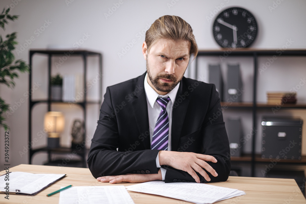 Mature bearded man dressed in stylish black suit sitting at desk with lots of documents. Concept of paperwork, finance and business. Mature bearded man dressed in stylish black suit sitting at desk with lots of documents. Concept of paperwork, finance and business.