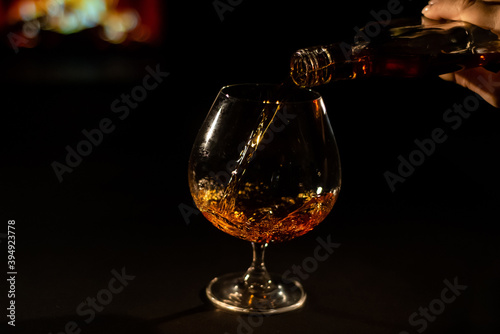 Close-up of a female hand with a glass of brandy on the background of the fireplace