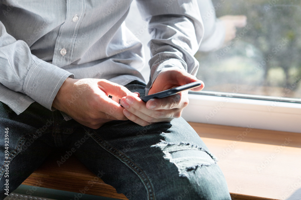 a man with a phone in his hands sits near the window