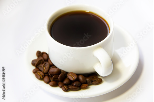 Close-up of coffee cup with roasted coffee beans on white background