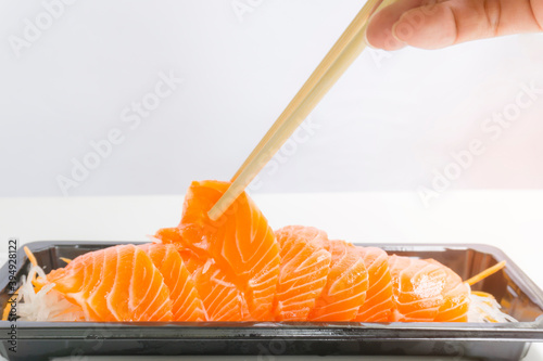 Salmon Sashimi on vegetable sliced in tray, bamboo chopsticks in hand